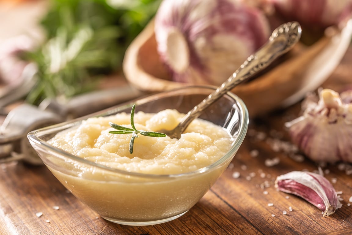 Garlic paste in a glass bowl with peeled garlic, salt, crusher and garlic heads